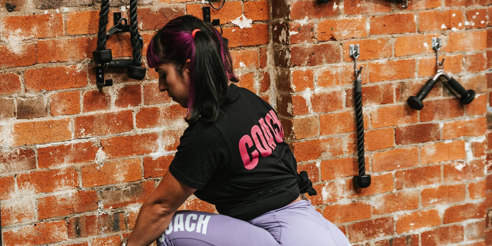 Romina doing a cable hip exercise against a brick wall