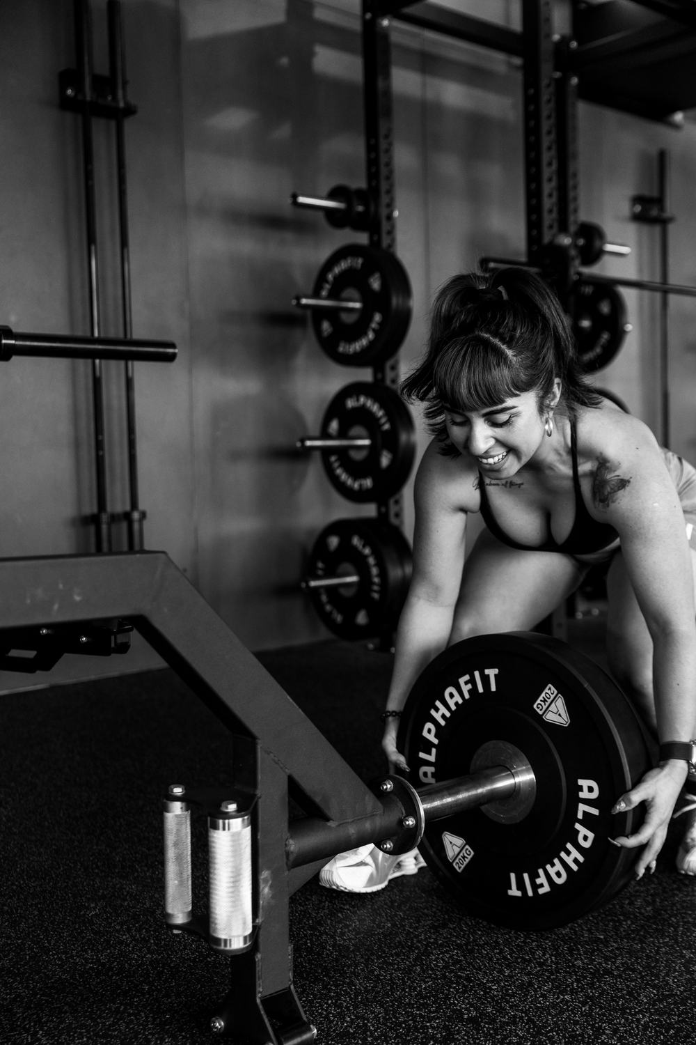Romina loading a plate onto a barbell, in black and white