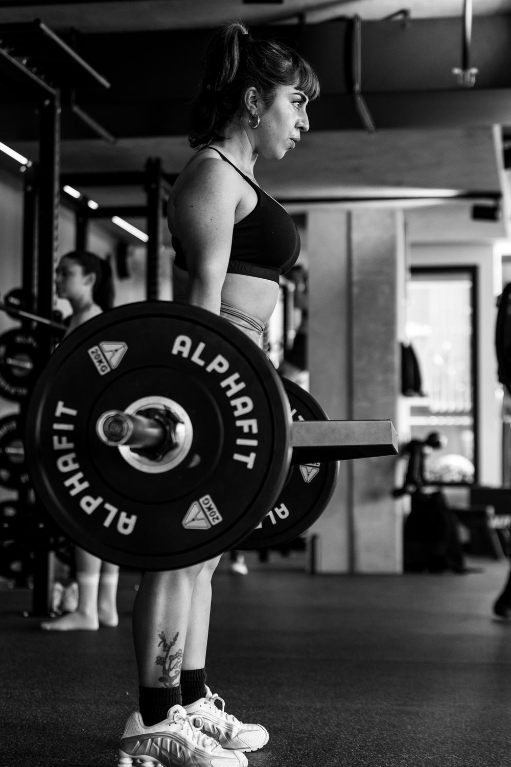 Romina beside a loaded barbell, in black and white